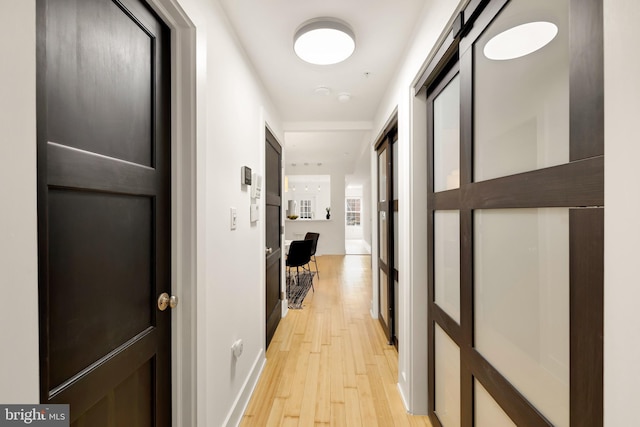 hall featuring light wood-style flooring and baseboards