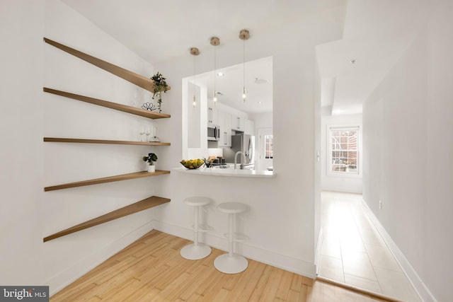 bar with pendant lighting, appliances with stainless steel finishes, light wood-type flooring, and baseboards