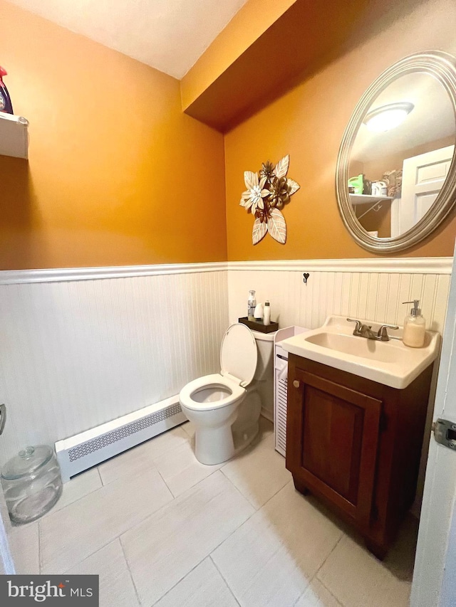 half bathroom with toilet, a wainscoted wall, baseboard heating, and vanity