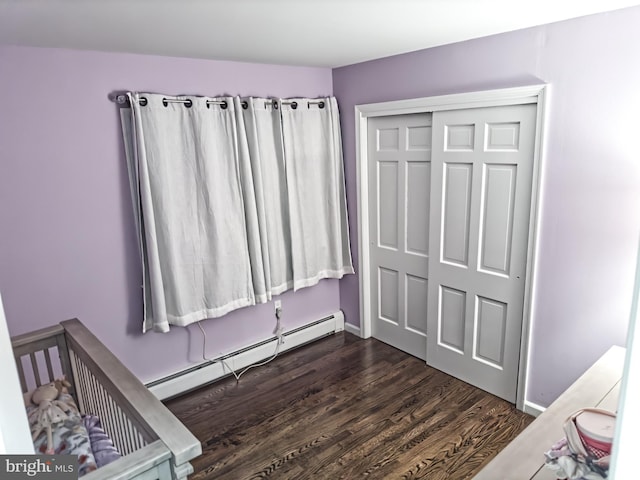 bedroom with dark wood-style flooring, baseboard heating, a closet, and baseboards