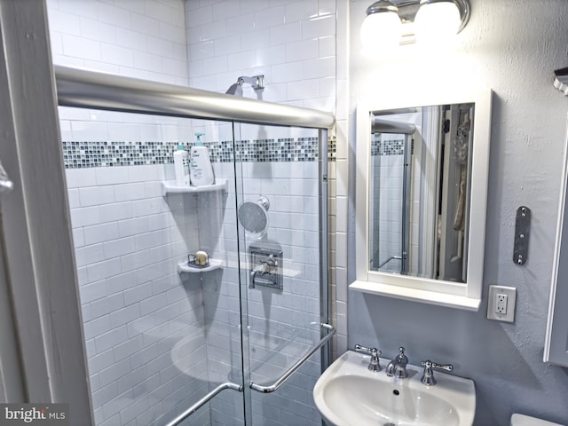 bathroom with a textured wall, a sink, and a shower stall