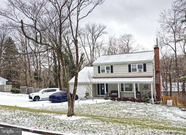 traditional-style house featuring a garage, a chimney, covered porch, fence, and central AC