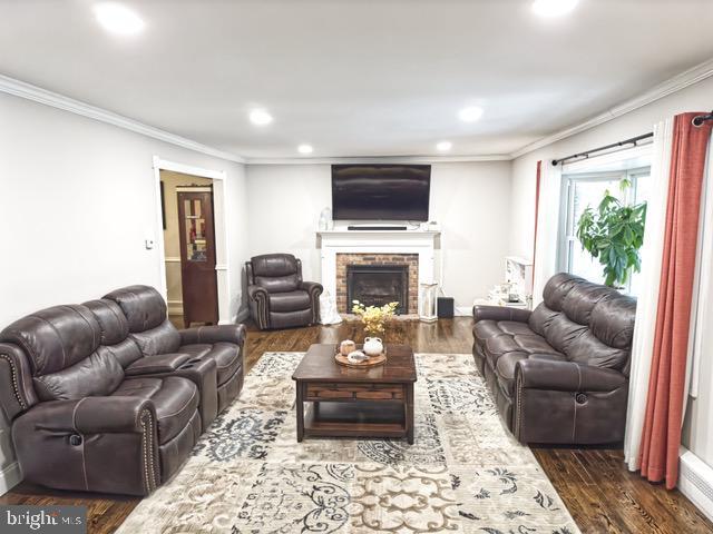 living room featuring a brick fireplace, crown molding, and dark wood-type flooring