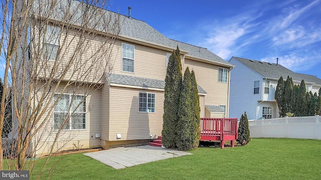 back of house with a lawn, roof with shingles, fence, a wooden deck, and a patio area