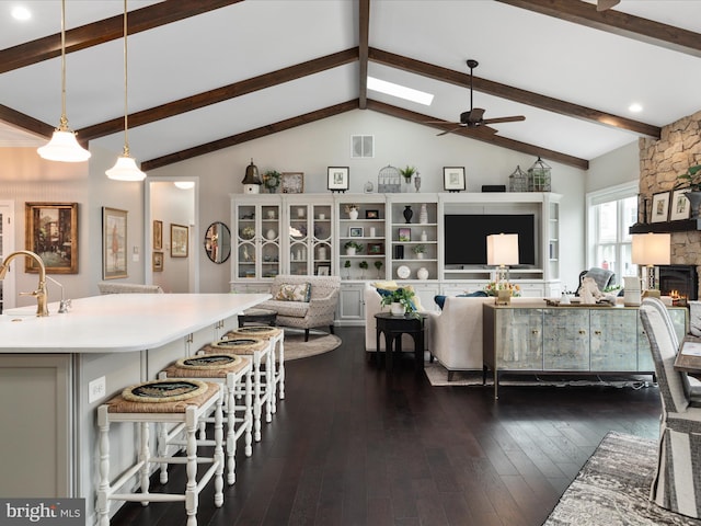 living room featuring vaulted ceiling with skylight, visible vents, ceiling fan, dark wood-type flooring, and a stone fireplace