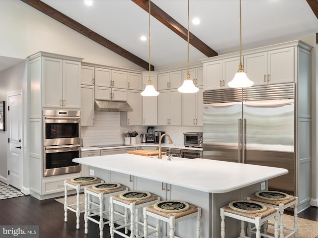 kitchen with vaulted ceiling with beams, tasteful backsplash, appliances with stainless steel finishes, under cabinet range hood, and a kitchen bar