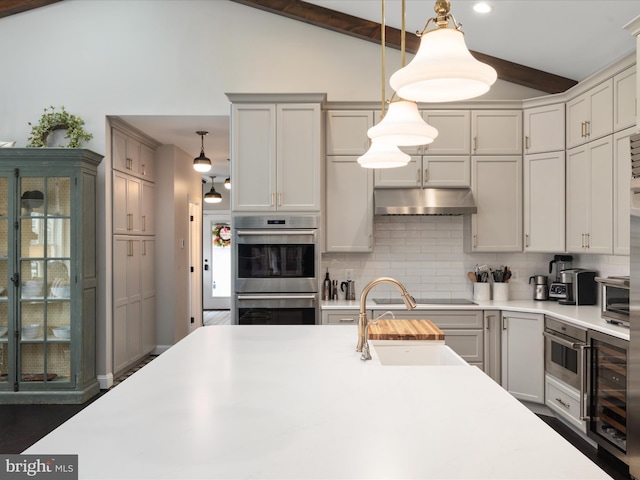 kitchen featuring wine cooler, backsplash, under cabinet range hood, double oven, and a sink