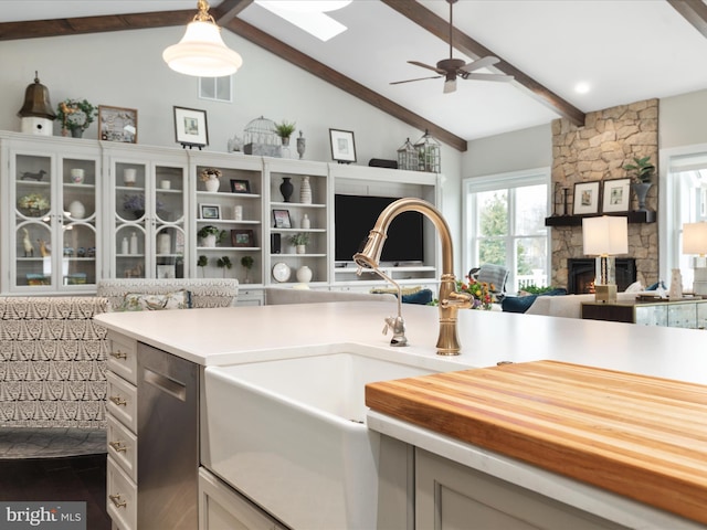 kitchen with vaulted ceiling with skylight, open floor plan, a stone fireplace, stainless steel dishwasher, and a sink