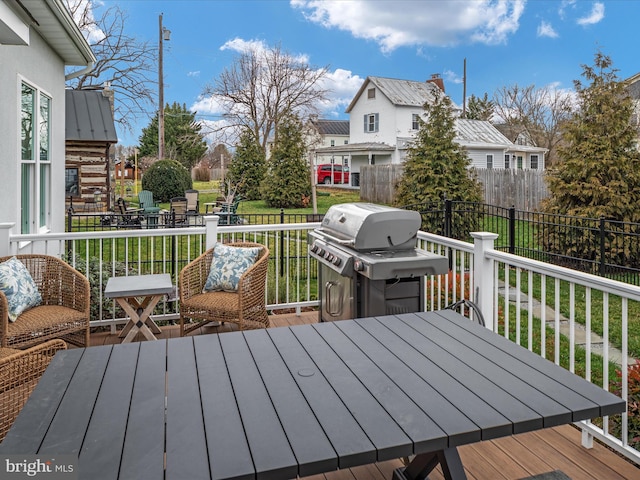 deck featuring outdoor dining space, fence, grilling area, and a lawn