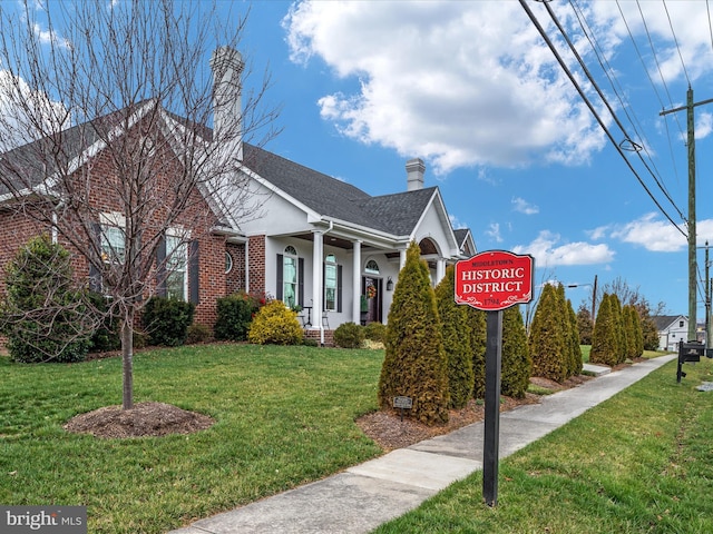 view of front of property featuring brick siding, roof with shingles, a chimney, stucco siding, and a front yard