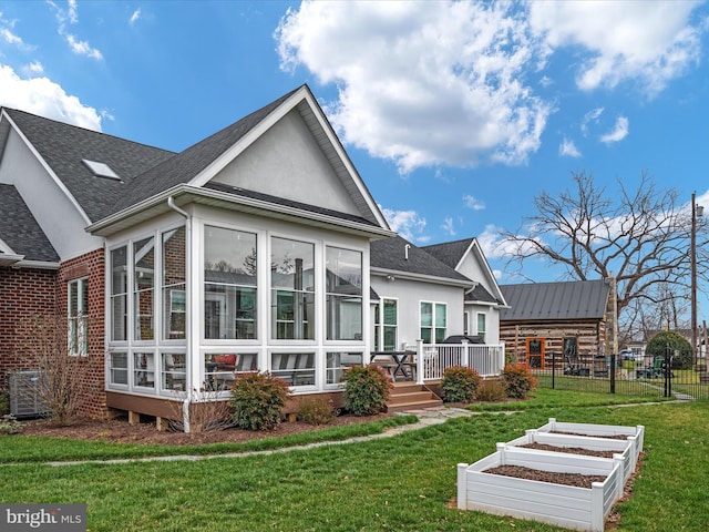 back of house featuring a vegetable garden, a sunroom, stucco siding, a yard, and brick siding