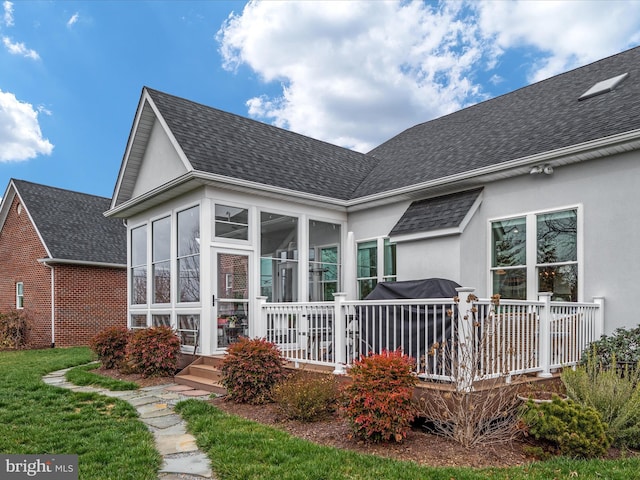 back of house featuring roof with shingles, a sunroom, and stucco siding