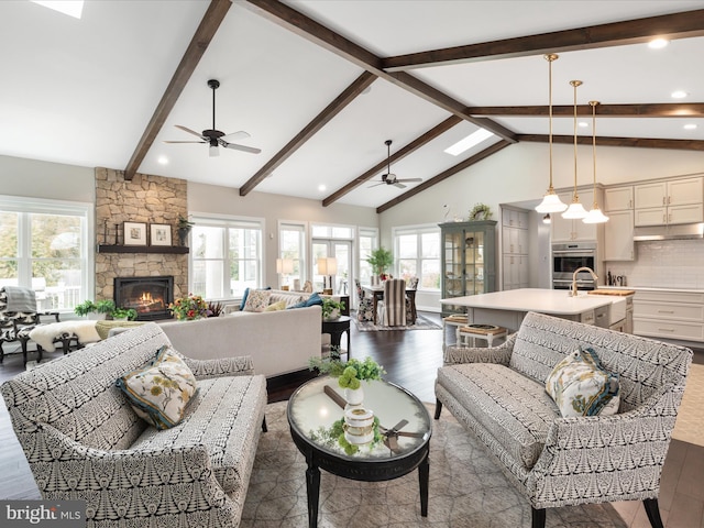 living room featuring ceiling fan, high vaulted ceiling, a stone fireplace, wood finished floors, and beamed ceiling