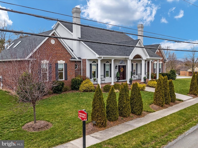 view of front facade featuring brick siding, roof with shingles, a chimney, stucco siding, and a front yard