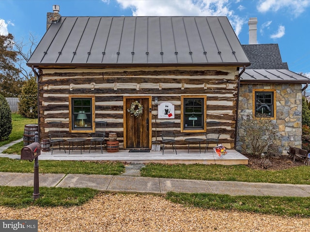 view of front of home featuring metal roof, stone siding, log exterior, a standing seam roof, and a chimney