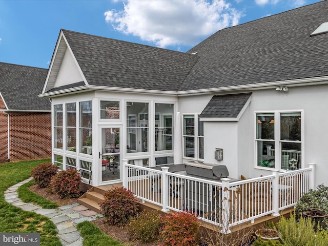 back of house with a sunroom, a shingled roof, and stucco siding