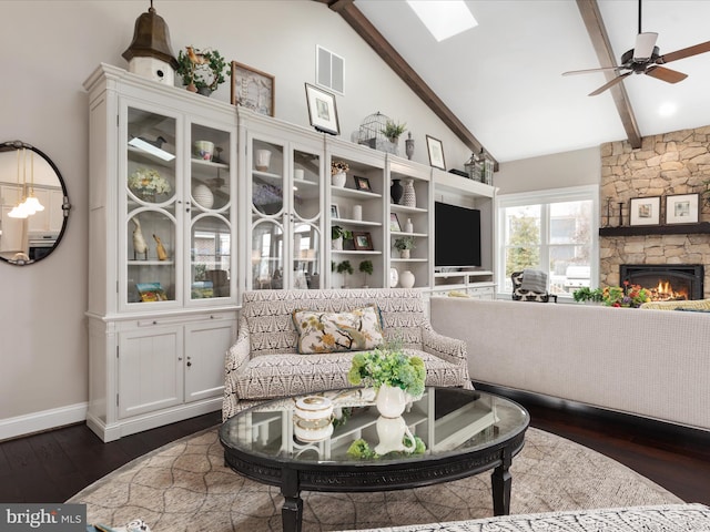 living area with visible vents, dark wood-style floors, ceiling fan, a stone fireplace, and beam ceiling