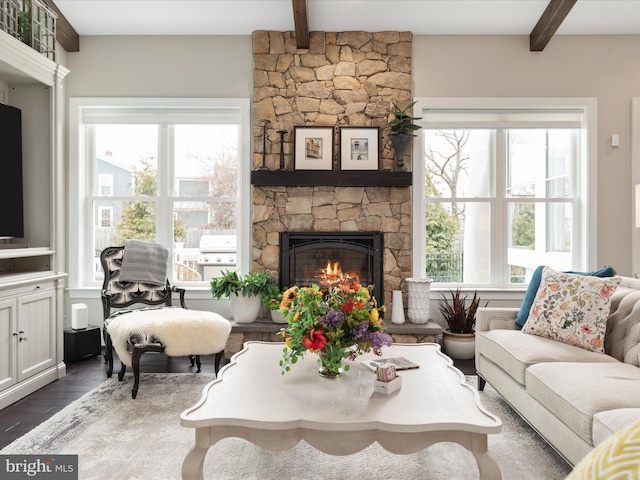 living room featuring a stone fireplace, beamed ceiling, and wood finished floors