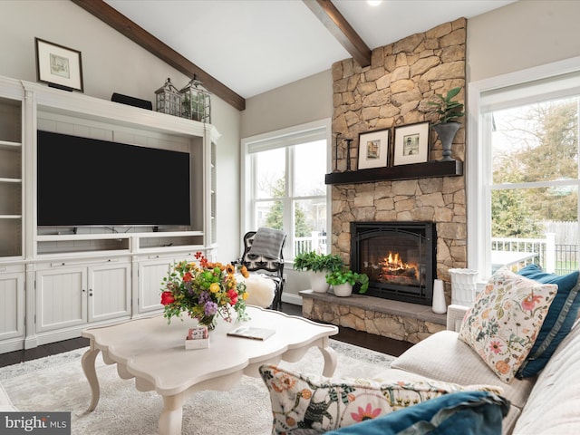 living room with lofted ceiling with beams, a stone fireplace, and wood finished floors