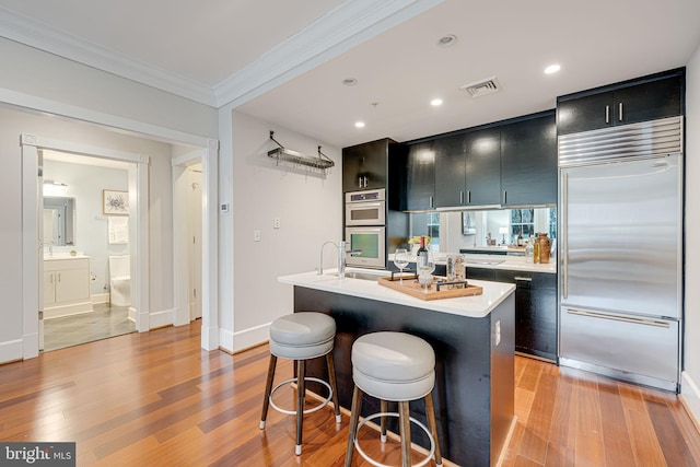 kitchen with visible vents, appliances with stainless steel finishes, a kitchen island with sink, light countertops, and dark cabinetry