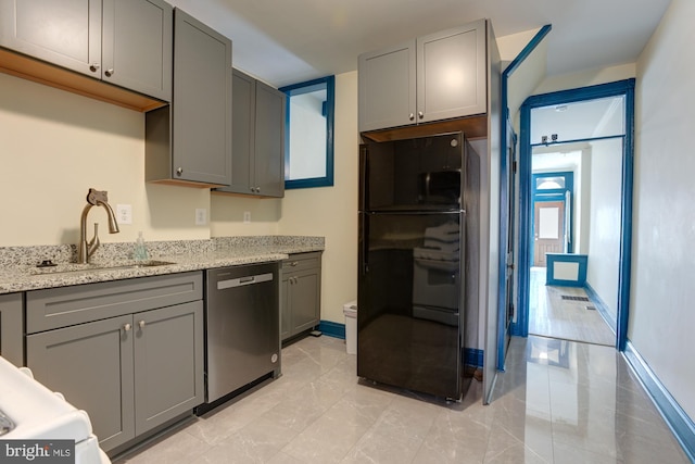 kitchen with light stone counters, gray cabinets, freestanding refrigerator, a sink, and dishwasher