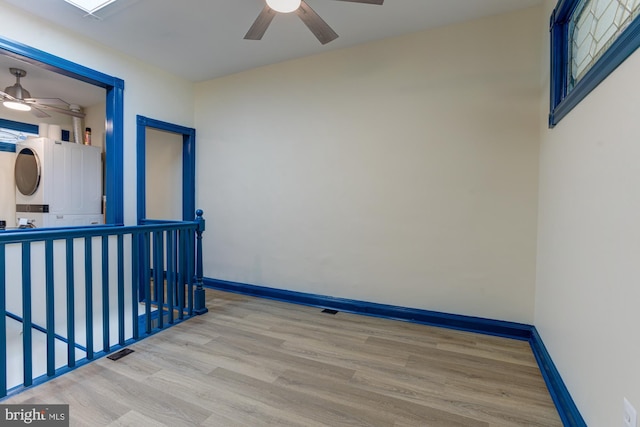 empty room featuring visible vents, baseboards, a ceiling fan, stacked washer and clothes dryer, and wood finished floors