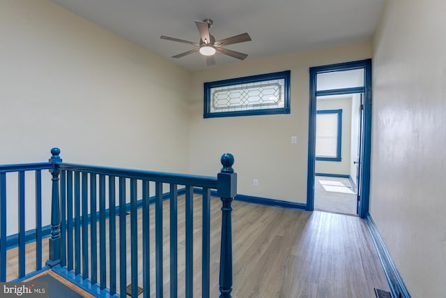 hall with baseboards, wood finished floors, and an upstairs landing