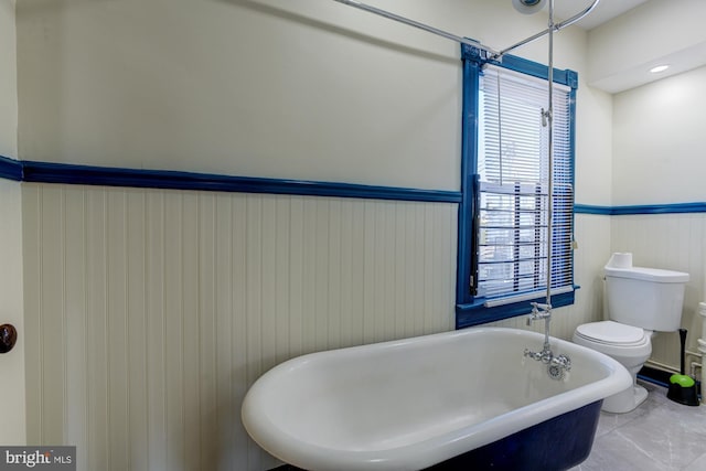 bathroom featuring toilet, a soaking tub, and a wainscoted wall