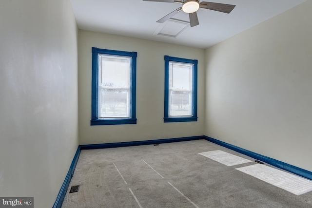 empty room with carpet, visible vents, attic access, a ceiling fan, and baseboards