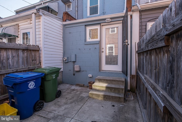 view of exterior entry with concrete block siding, a patio area, and fence