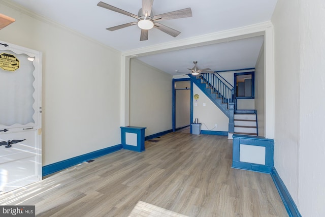 unfurnished living room featuring wood finished floors, a ceiling fan, baseboards, stairway, and crown molding