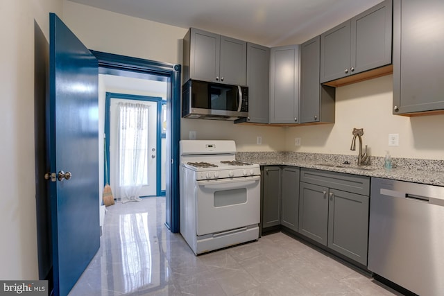 kitchen featuring light stone countertops, appliances with stainless steel finishes, gray cabinets, and a sink