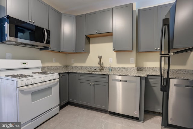 kitchen featuring white gas range, gray cabinetry, freestanding refrigerator, a sink, and dishwasher