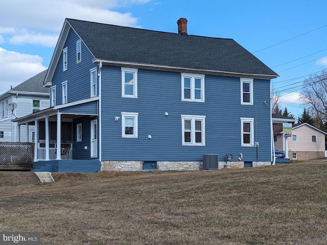 rear view of property featuring central AC unit, a chimney, roof with shingles, a yard, and a porch