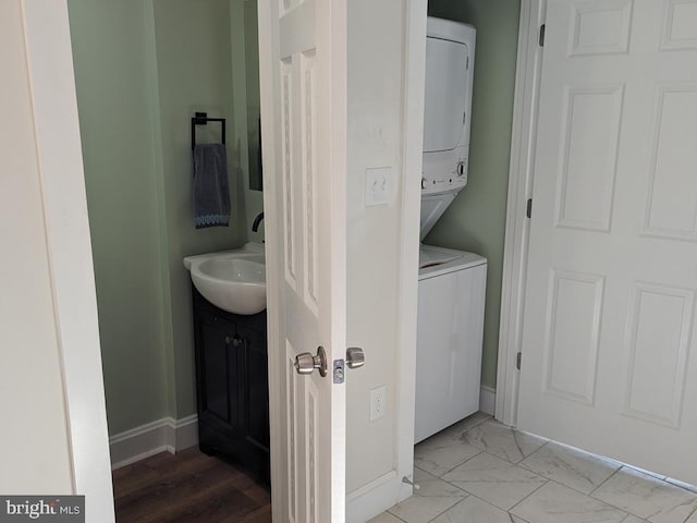 washroom with laundry area, baseboards, stacked washer / drying machine, marble finish floor, and a sink