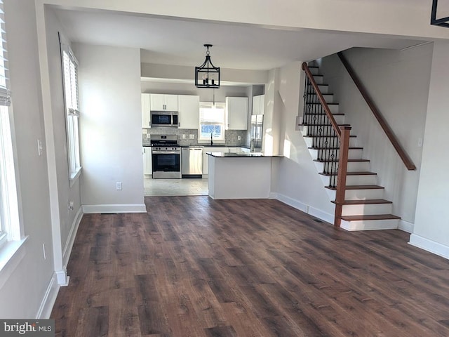 kitchen featuring dark wood finished floors, stainless steel appliances, decorative backsplash, white cabinets, and baseboards