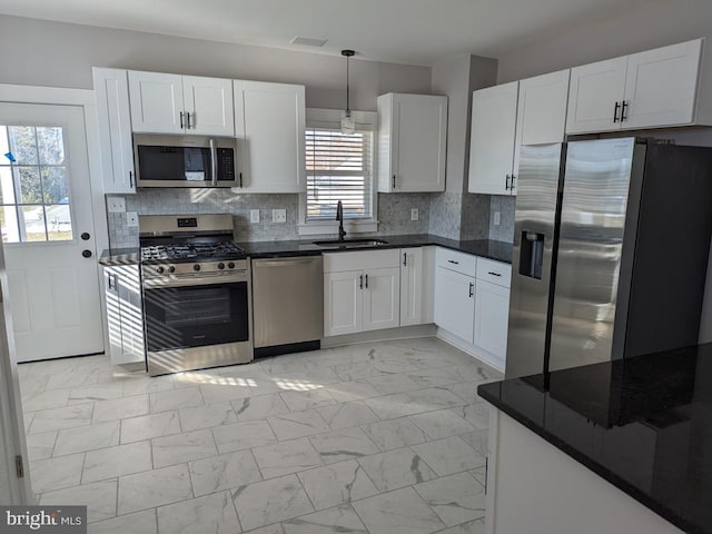 kitchen featuring white cabinets, dark countertops, marble finish floor, stainless steel appliances, and a sink