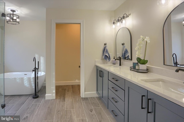 bathroom with wood tiled floor, a soaking tub, a sink, and double vanity