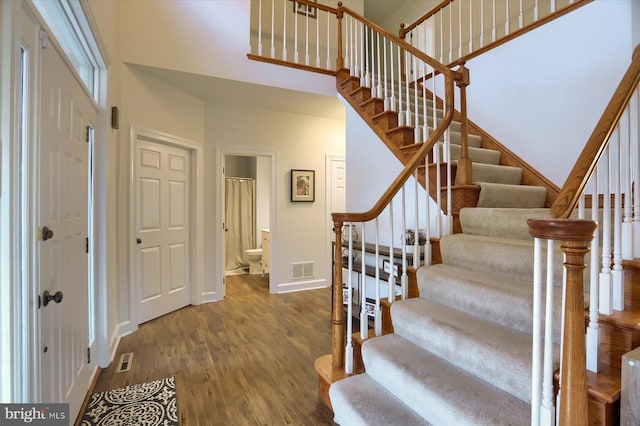 staircase featuring baseboards, visible vents, a high ceiling, and wood finished floors