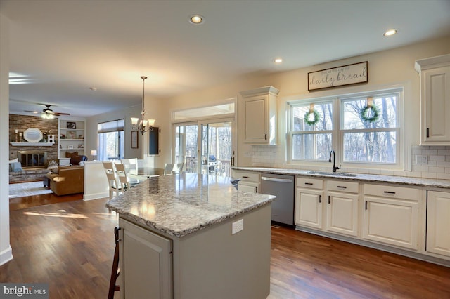 kitchen with a center island, a fireplace, stainless steel dishwasher, open floor plan, and a sink