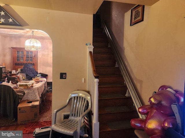 stairs featuring arched walkways and wood finished floors