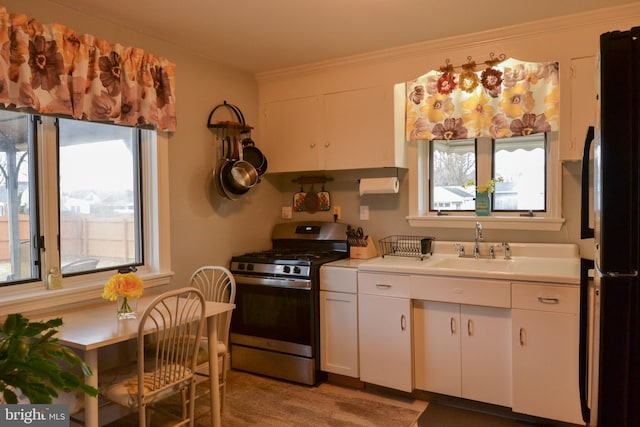 kitchen with crown molding, light countertops, freestanding refrigerator, stainless steel gas stove, and white cabinetry