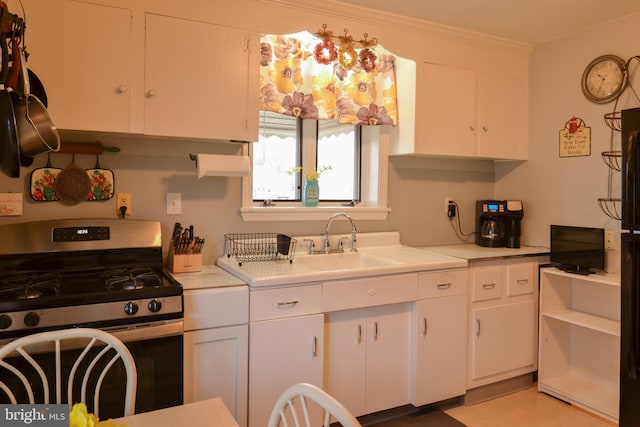 kitchen with stainless steel range with gas cooktop, crown molding, light countertops, white cabinetry, and a sink