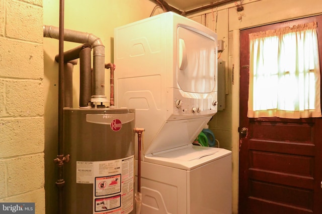 laundry room with concrete block wall, laundry area, gas water heater, and stacked washer / dryer