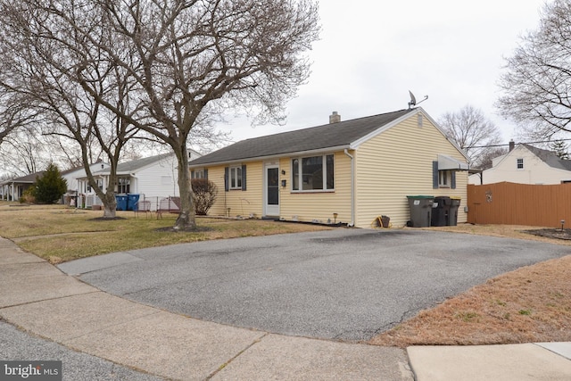 view of front of property with aphalt driveway, a chimney, a shingled roof, a front yard, and fence