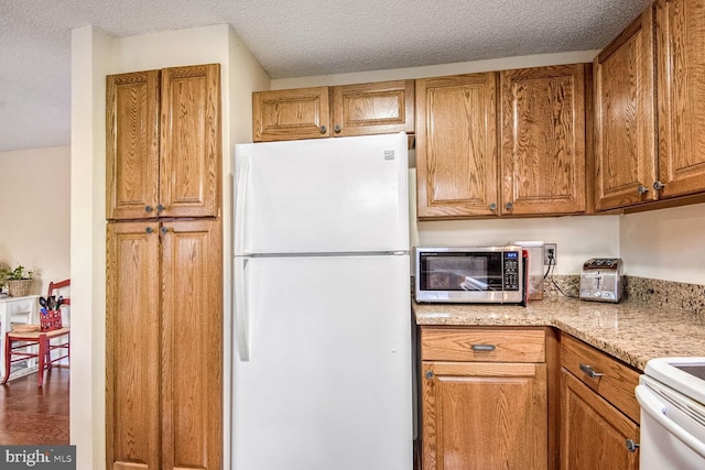 kitchen featuring brown cabinets, freestanding refrigerator, stainless steel microwave, and a textured ceiling