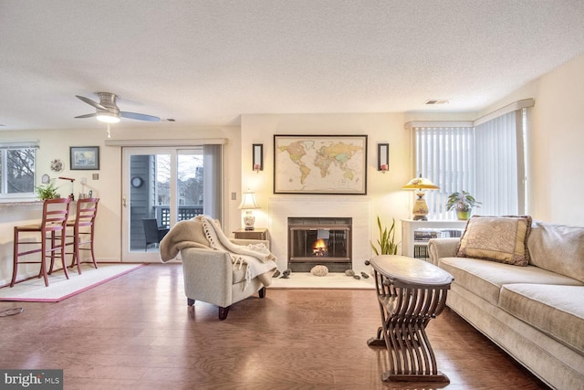 living area with a textured ceiling, visible vents, wood finished floors, and a glass covered fireplace