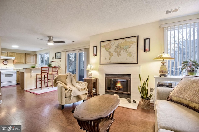 living area with a textured ceiling, a glass covered fireplace, dark wood finished floors, and visible vents