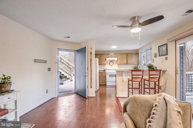 kitchen featuring white appliances, visible vents, dark wood-style floors, a breakfast bar, and light countertops