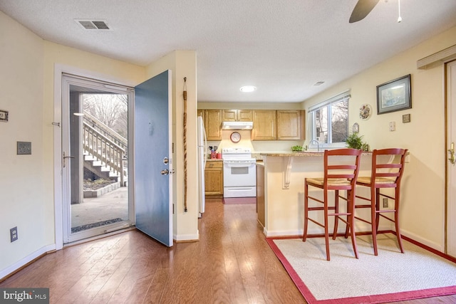 kitchen with white appliances, visible vents, a kitchen breakfast bar, dark wood-style flooring, and under cabinet range hood